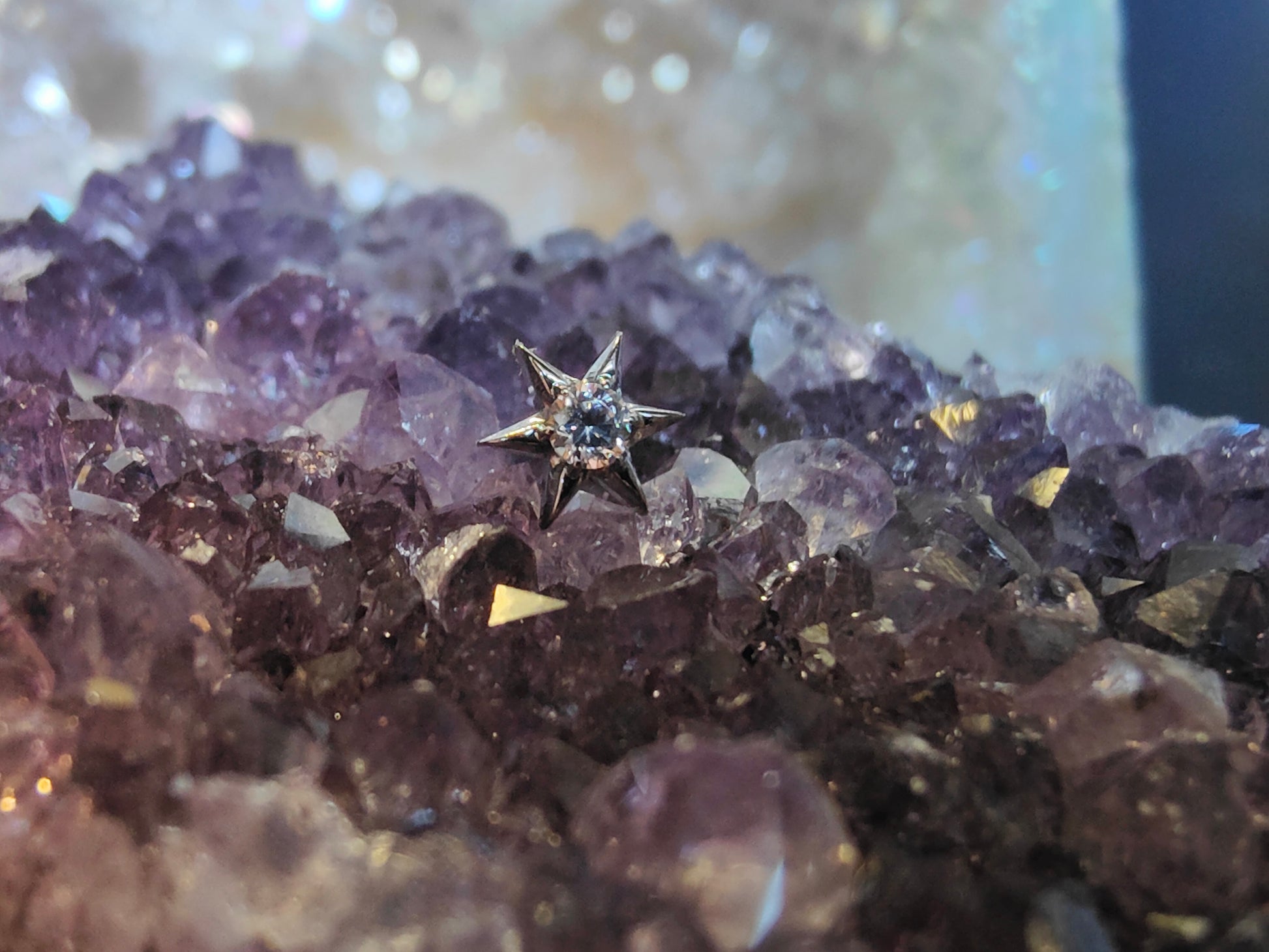 6 point titanium star with a white gem in the centre, sat on an amethyst crystal