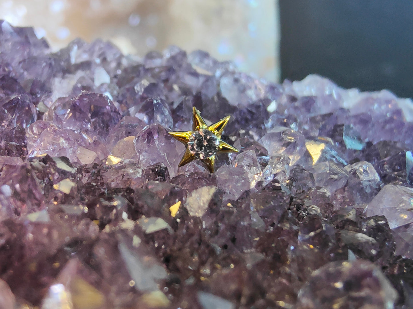 6 point yellow colured titanium star with a white gem in the centre, sat on an amethyst crystal