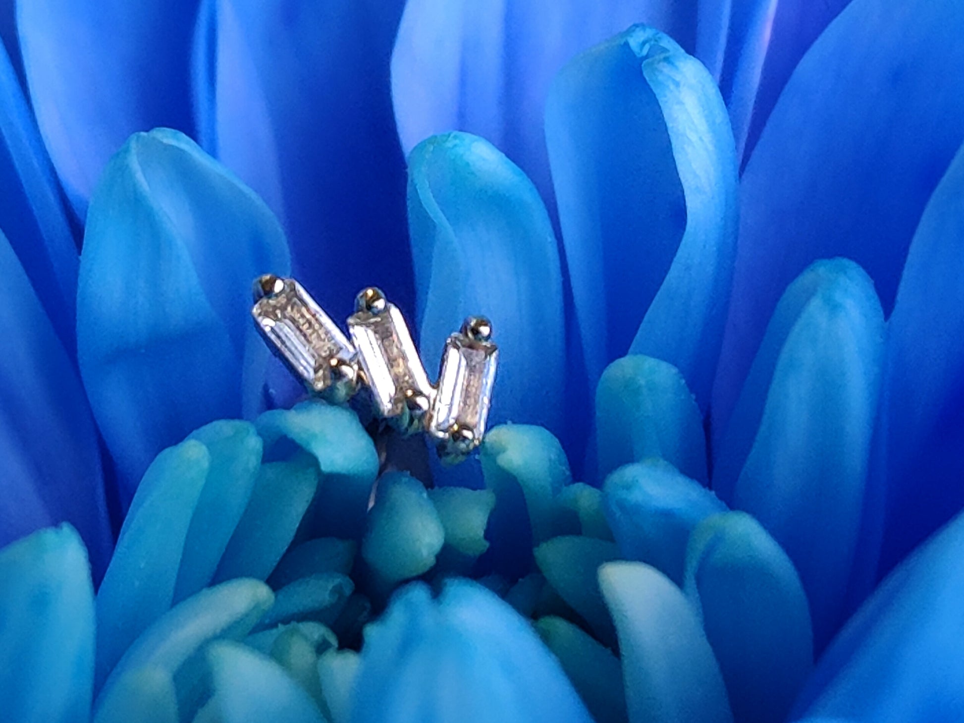 3 baguette cut topaz stones set in gold. sat on a blue flower