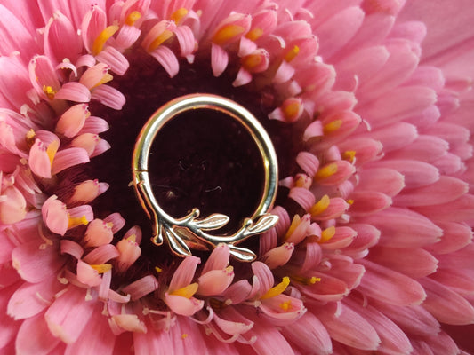 a solid gold ring with a leaf design. sat on a pink flower