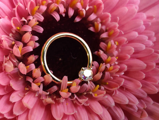 a yellow gold seam ring with a 3mm prong set stone in mercury mist topaz. sat on a pink flower