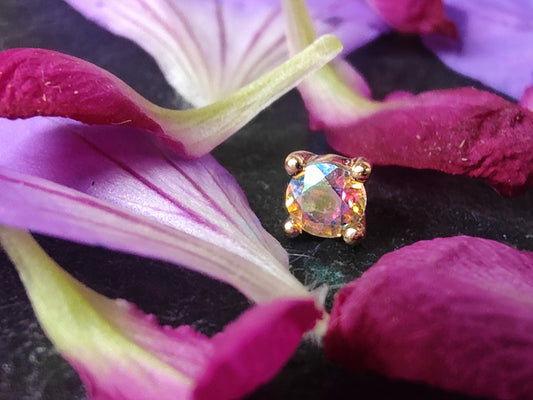 a solid gold prong set stone with mercury mist topaz surrounded by pink and purple petals. 
