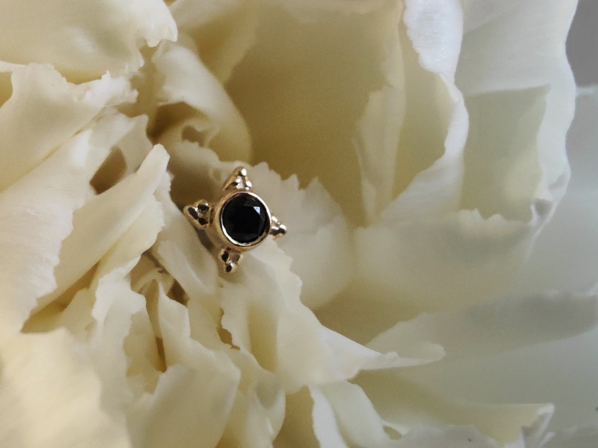 an onyx stone with 4 tri bead accents in yellow gold sat on a white flower