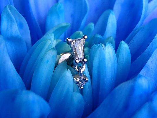 a tapered baguette cut piece with a dangly charm in white CZ sat on a blue flower