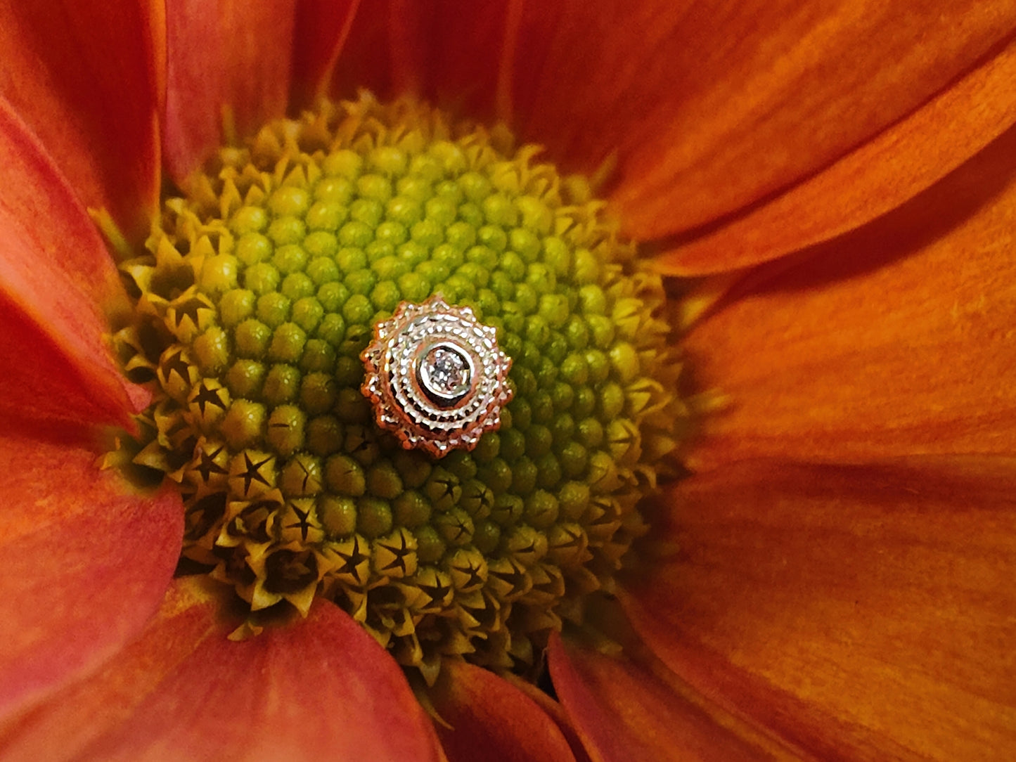 a milligrain mandala shaped end in yellow gold with a diamond centre stone sat on an arange flower