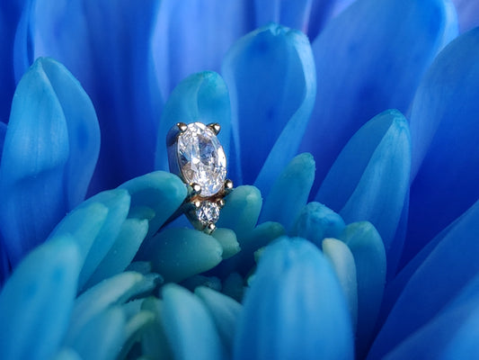 a yellow gold end withone larger oval stone and a lower smaller circle stone placed on a bright blue flower