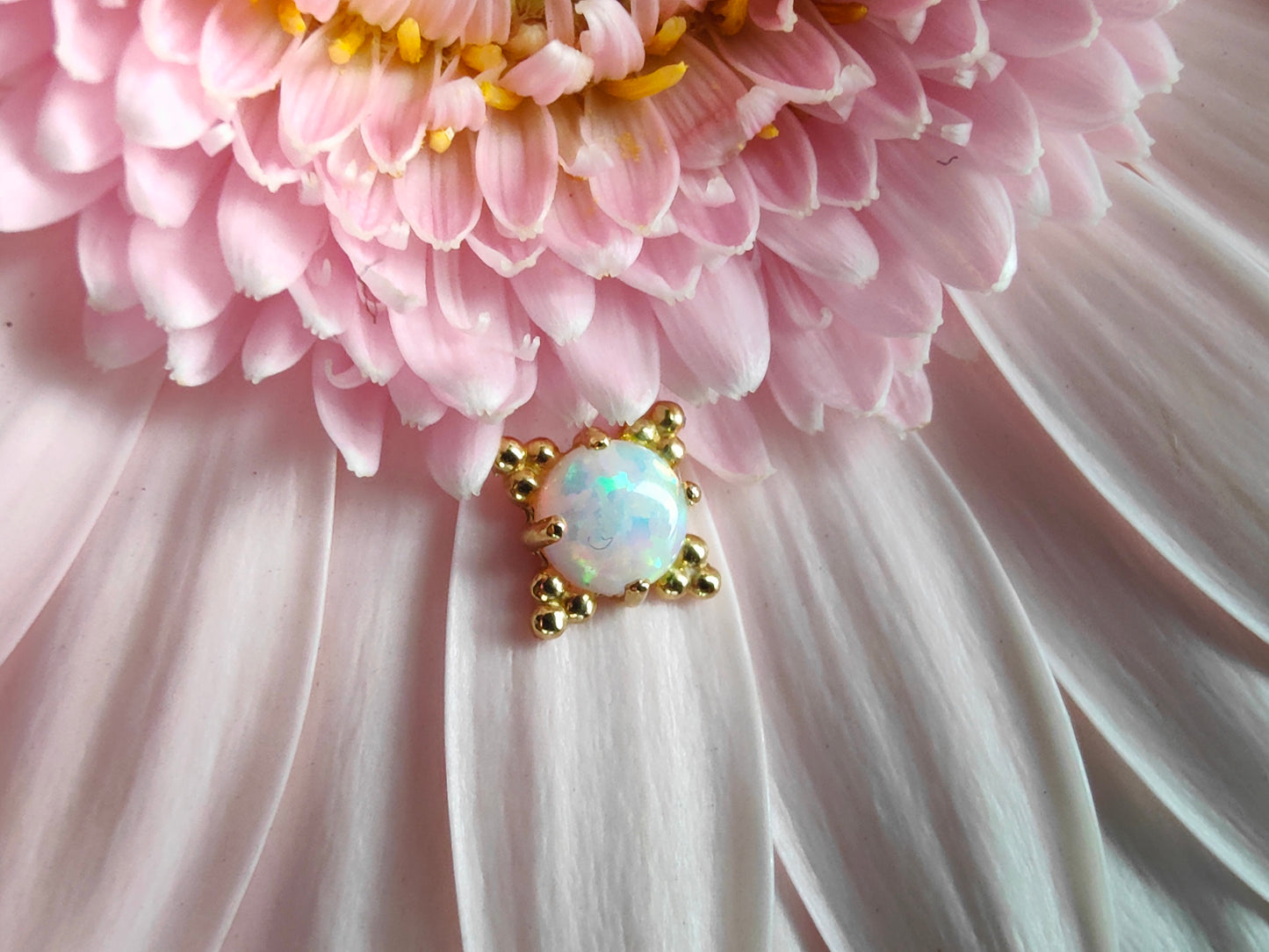 solid gold beaded end with an opal centre stone placed on a light pink flower