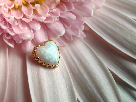 an opal heart end in a yellow gold prong setting, places on a pink flower